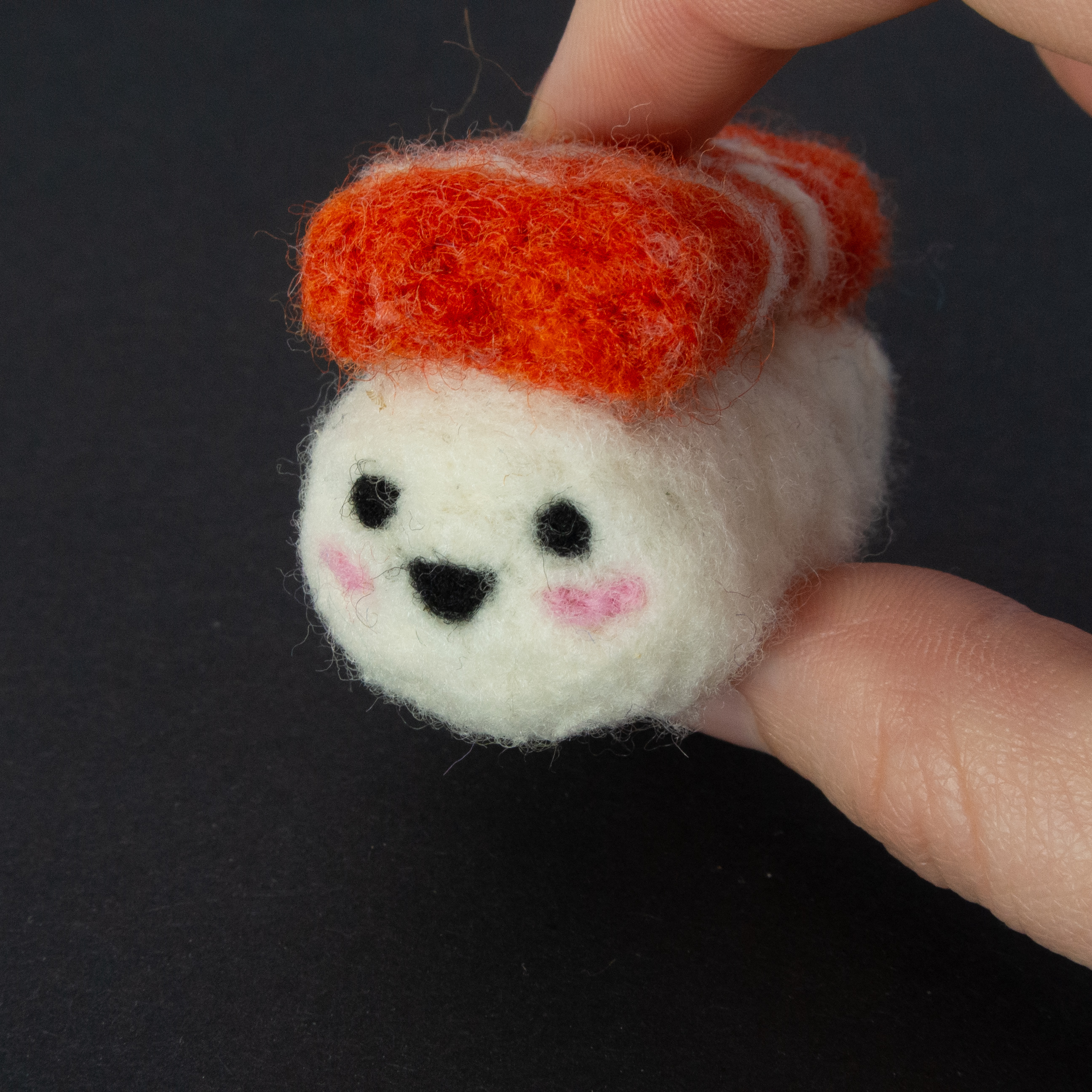 Gefilzte Sushirolle mit lächelndem Gesicht zwischen Daumen und Zeigefinger gehalten